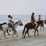 Group of people enjoying horseback riding along Bucerías beach, Mexico, against ocean waves.